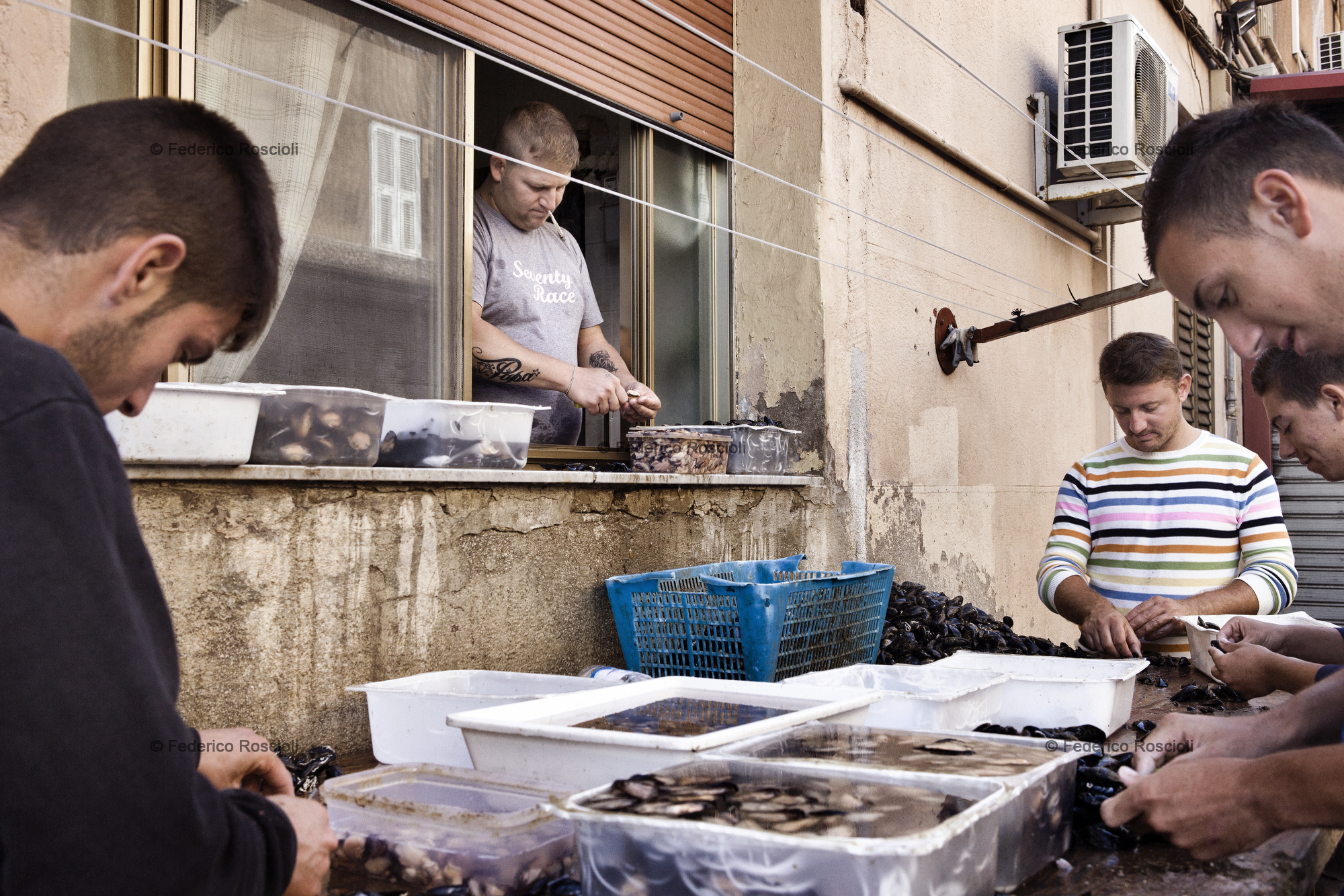 Taranto, Italy, September 26, 2013. Armando and his friends cleaning mussels in Citt Vecchia. Armando works form the window of is house because is under house arrest. In 2012, due to high levels of dioxin and Pcb, 20 tons of mussels were destroyed, half of the yearly production. Actually it is forbidden to cultivate mussels in Mar Piccolo. Doing so, all the environmental characteristics that gave the unicity to the Tarantinian mussels are lost.